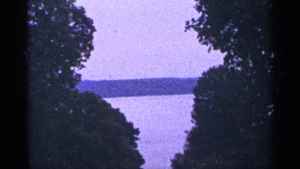 Handheld 1964 Washington, DC landscape frame showing trees around a hazy lake and low far shore.