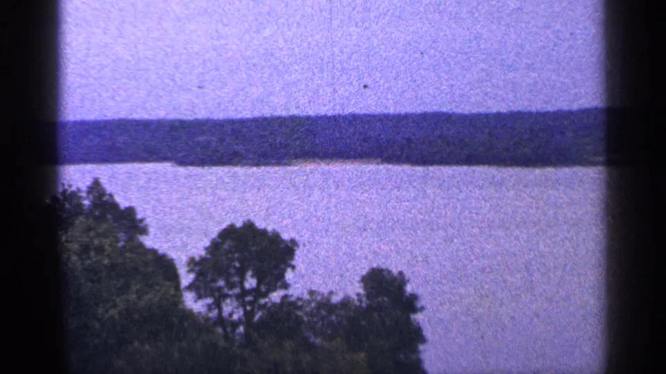 1964 Washington, DC 8mm frame looking over foreground trees toward open water and a distant wooded shoreline.