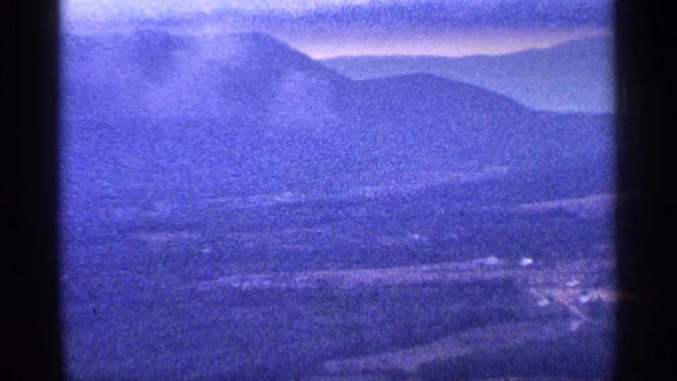 Visitor-shot 8mm view across hazy mountain ridges and a broad valley, with soft focus and blue-tinted film color.