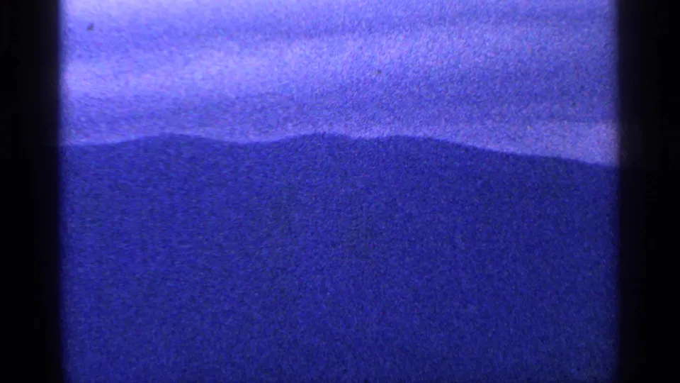 1964 8mm home-movie view of a dark mountain silhouette below a cloudy, blue-shifted sky, with soft focus and visible grain.