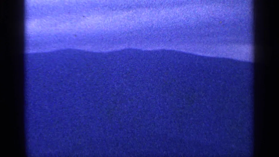 Blue-cast 1964 8mm frame showing a broad mountain ridge under overcast sky, bordered by dark film gate shadows.