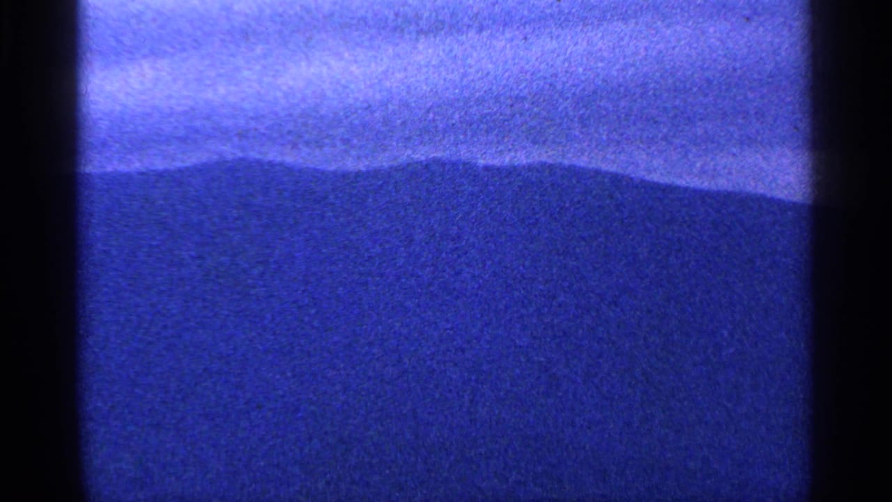 1964 8mm frame from Washington DC showing a blue exposed field, dark horizon-like shape, grain, and film gate edge.
