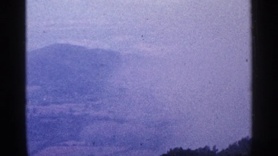 Hazy mountain ridge and pale sky in a 1964 8mm frame, bordered by dark vertical film or obstruction edges.