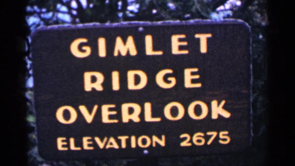 1964 8mm frame showing a Gimlet Ridge Overlook sign with elevation 2675, set against trees and dark film edges.