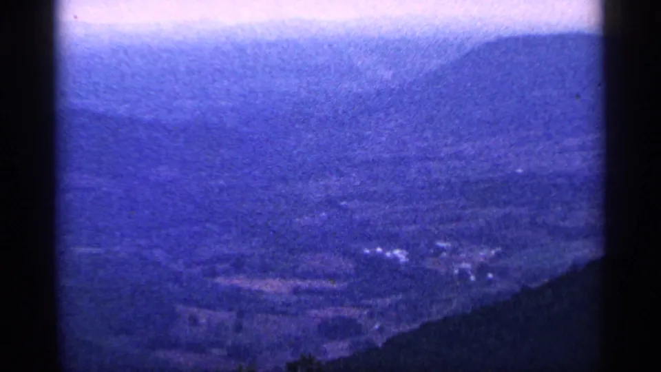 Final 8mm frame of the overlook panorama, with blue haze, distant ridge lines, and a dark slope in the foreground.