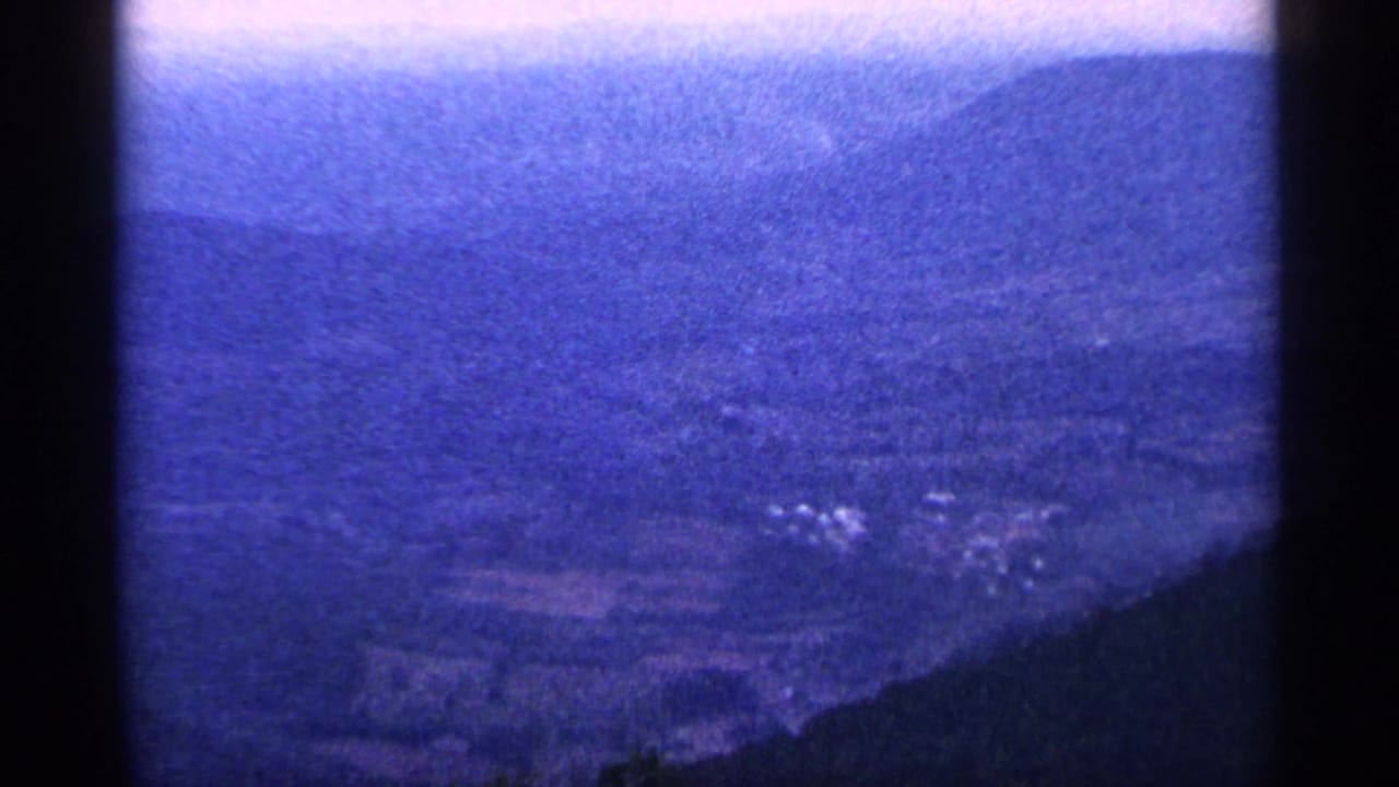 Blue-tinted distant hillside and dark foreground tree line on vintage film.
