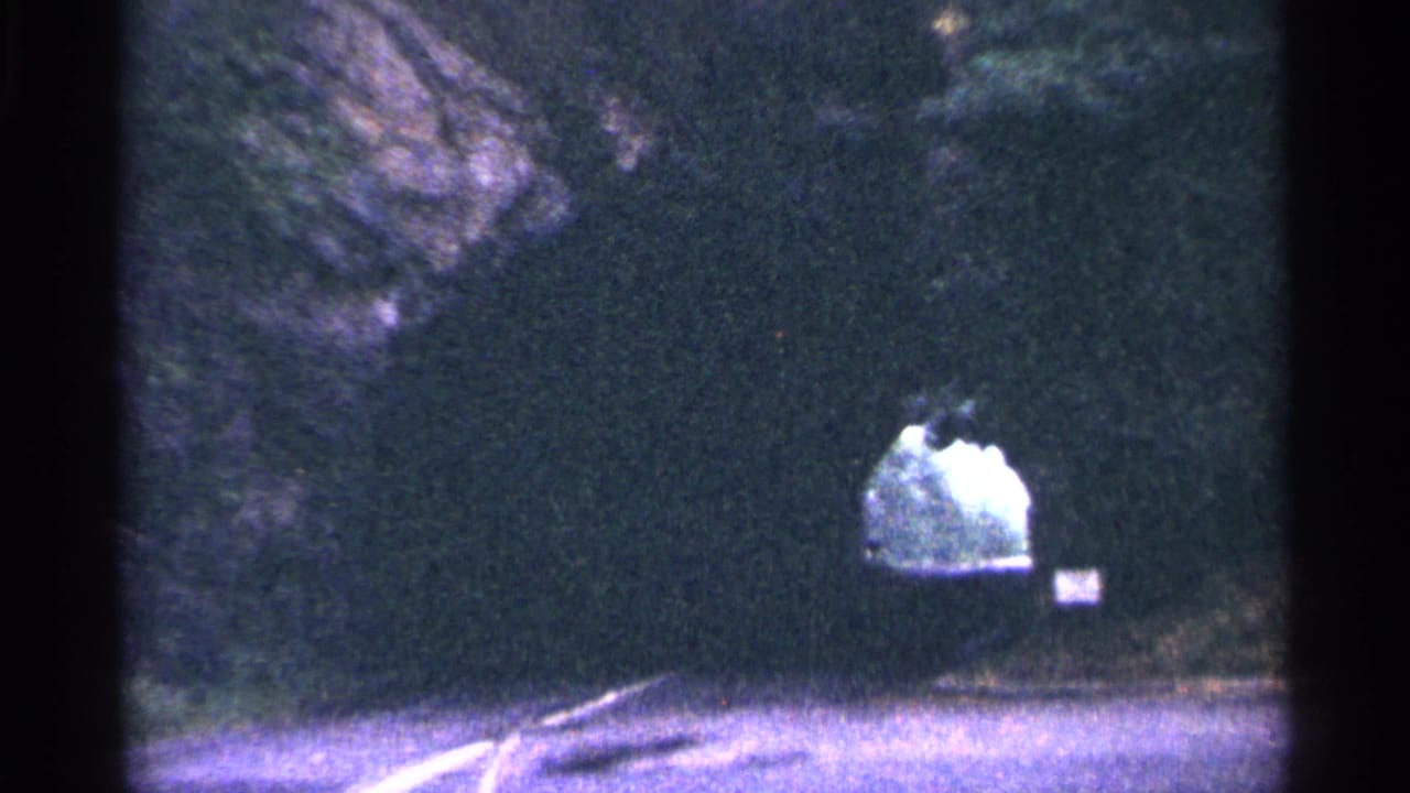 1964 West Virginia 8mm frame showing a road approaching a dark tunnel cut through rock, with bright daylight visible at the far end.