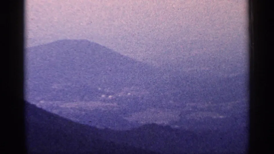 1964 West Virginia 8mm frame of hazy layered mountains, a dark foreground ridge, and faint valley detail softened by exposure and grain.