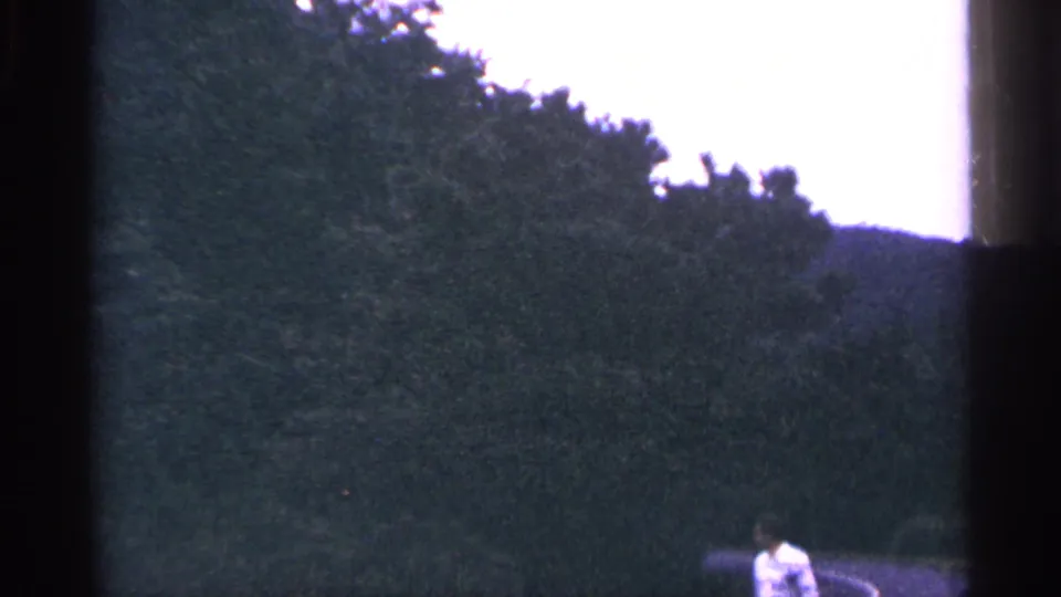 1964 West Virginia roadside view with dense trees, low hills, a curved road, and an adult man partly visible at the bottom of frame.