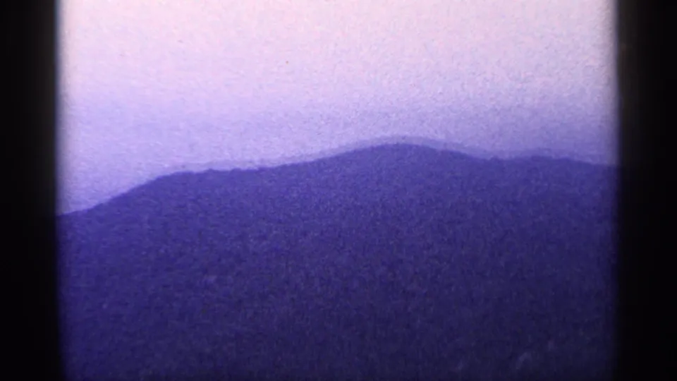 A blue-tinted mountain ridge fills the frame under a pale sky, consistent with the West Virginia home-movie landscape sequence.