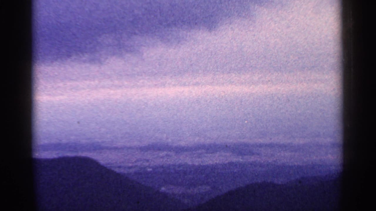1964 West Virginia home-movie frame showing layered mountain silhouettes under a hazy purple-blue sky.