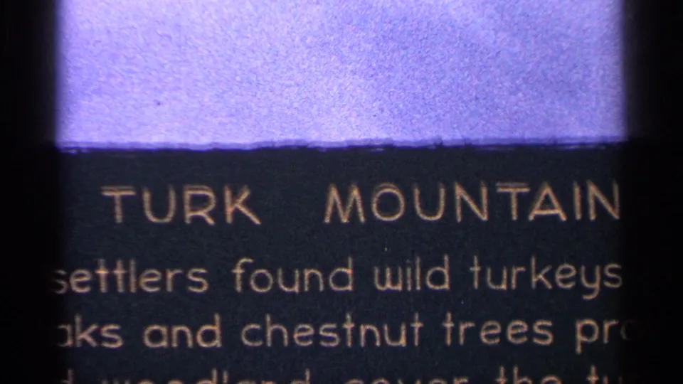 Title card for Turk Mountain with partial text about settlers, wild turkeys, and trees visible on 8mm film.