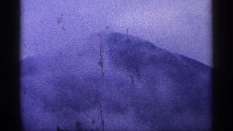 1964 West Virginia 8mm frame with a hazy mountain slope, purple color shift, visible grain, scratches, and dark vertical frame border.
