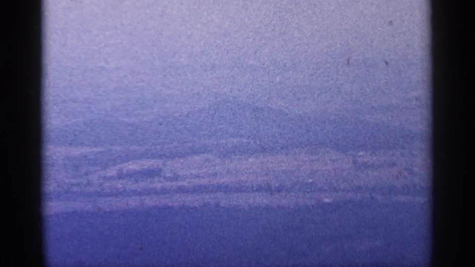 Purple-tinted 8mm landscape frame showing distant layered West Virginia ridges under a pale hazy sky.