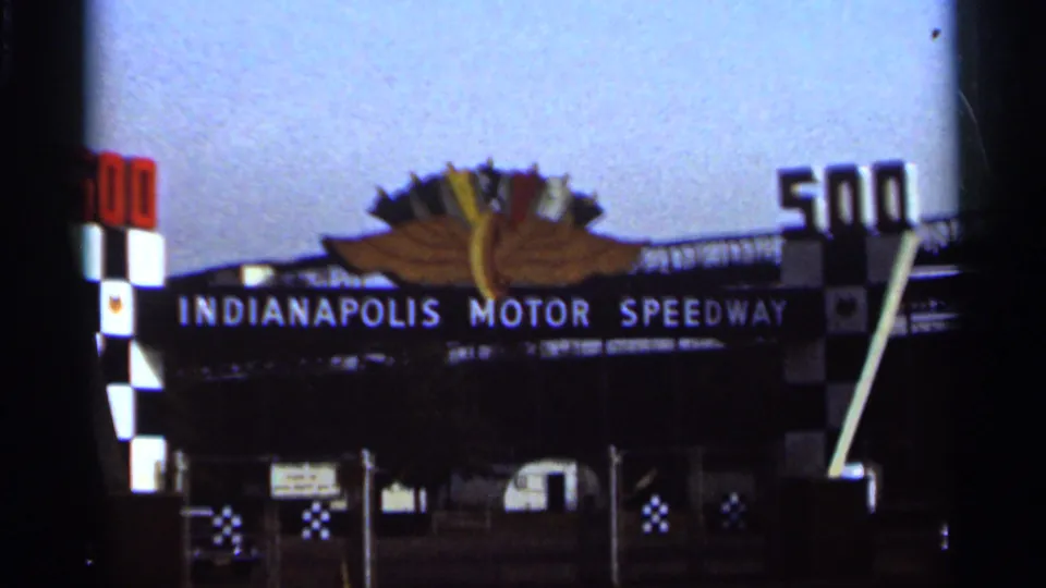 8mm frame showing Indianapolis Motor Speedway signage, checkered entrance columns, and large 500 numerals above the gate.