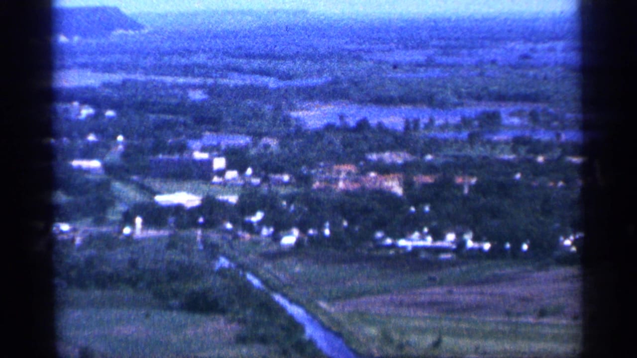 Elevated 1965 Duluth-area view with tree cover, low buildings, fields, and a blue hazy horizon.