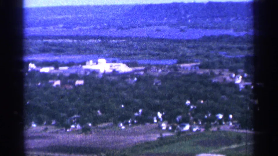 1965 Duluth-area 8mm frame with wooded homes below, bright buildings mid-frame, and hazy distance.