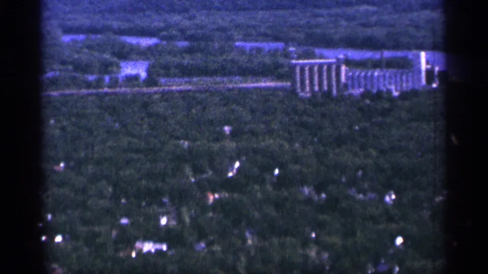 1965 Duluth aerial 8mm frame showing wooded residential areas with a long grain-elevator-like structure in the distance.