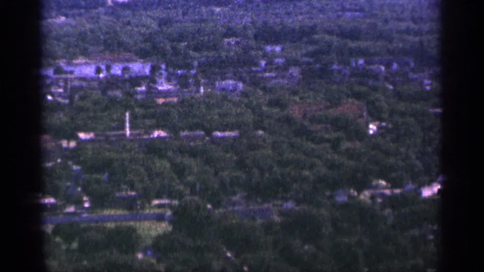 1965 Duluth frame looking over a broad canopy of trees with homes, roads, and low buildings spread across the town.