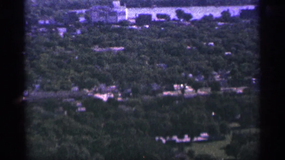 1965 Duluth frame showing a wooded townscape with small structures and roads softened by grain and purple-blue color shift.