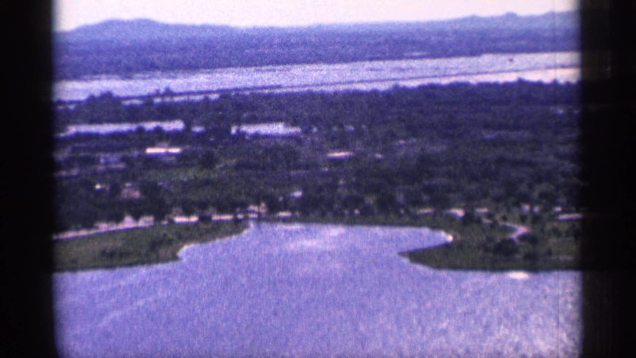 High view over a lake, small settlement, trees, and distant hills.