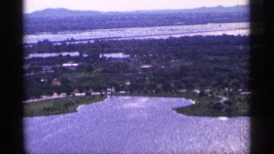 1965 Duluth-area home-movie view looking down over shoreline water, scattered buildings, trees, and distant ridges.
