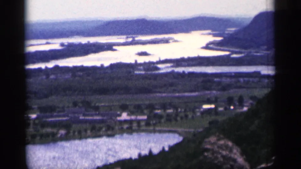 Elevated 1965 Duluth, Minnesota view of reflective waterways, green shoreline, roads, and low wooded hills.