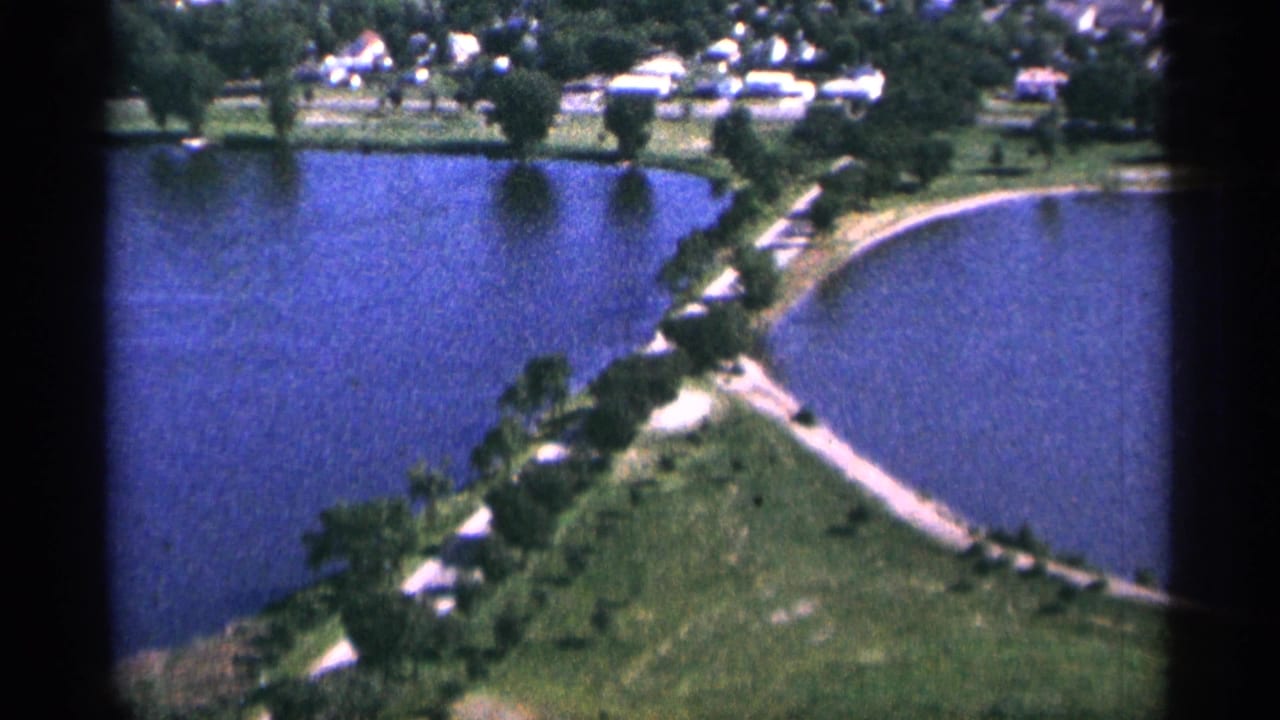 Aerial view of two blue water areas divided by a tree-lined strip and shoreline paths.