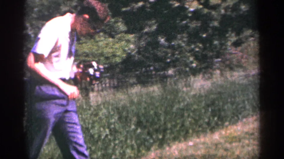 The man holds a camera at his side while walking or looking down on a grassy Duluth hillside path bordered by summer greenery.