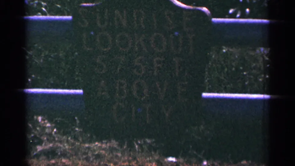 Close 1965 home-movie view of a weathered Duluth Sunrise Lookout sign with partially legible height text.