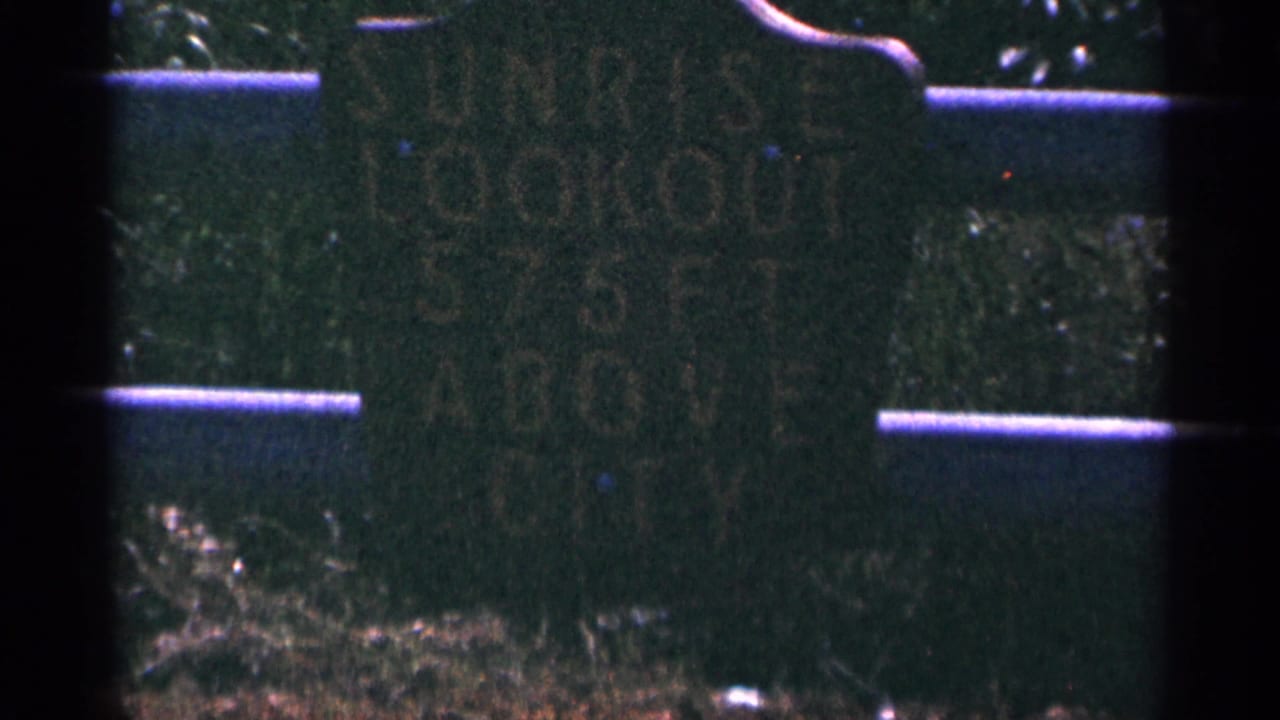Weathered Sunrise Lookout sign mounted on a wooden fence in dark 8mm footage.