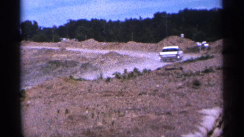 A white car travels through a dusty construction area in Duluth, Minnesota, in 1965 home-movie footage.