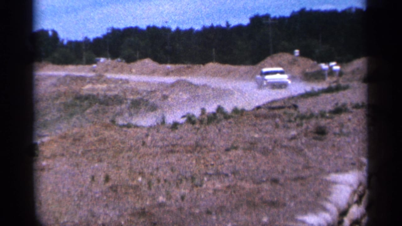 The car moves farther along the dusty construction path, framed by excavated earth and a dark treeline in Duluth.