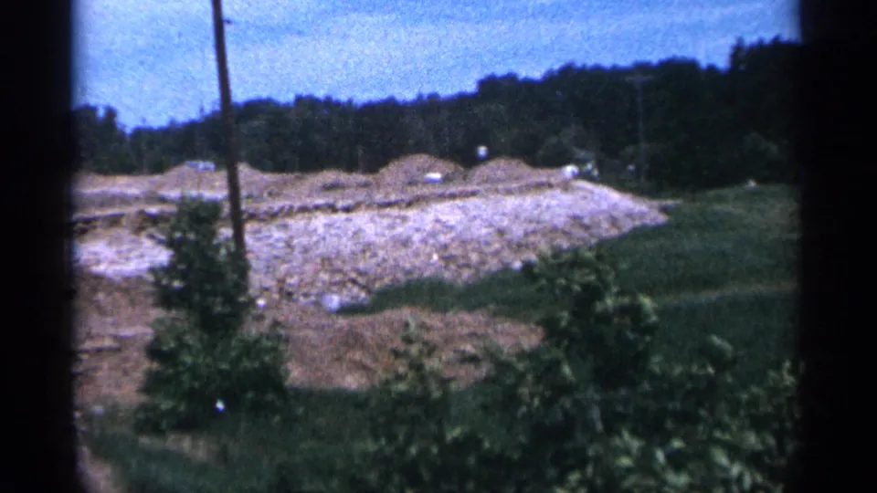 A wider view of the Duluth construction area shows rough ground, a utility pole, vegetation, and small distant vehicles.
