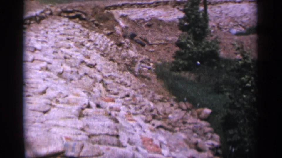 Closer 1965 Duluth view of pale rocks, exposed soil, grass, and a small tree along the embankment edge.