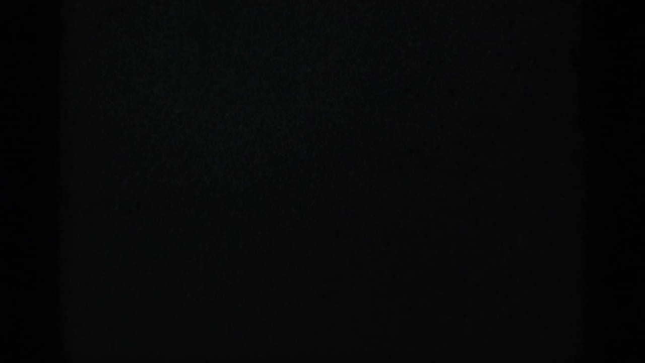 Mostly dark film frame with faint texture and heavy edge shadow.