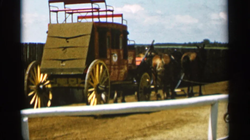1965 Duluth 8mm frame showing a western-style stagecoach with horses on a dirt lot behind a low barrier.