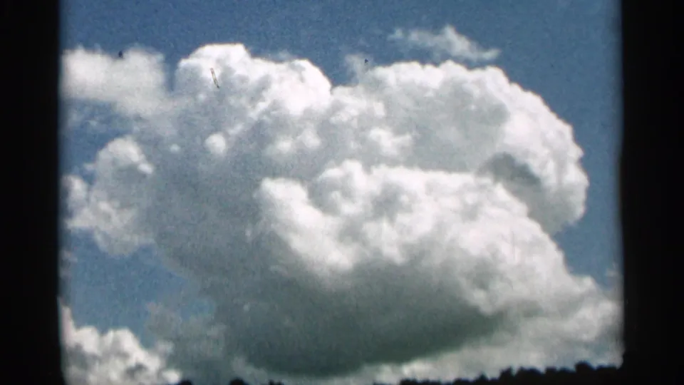 1965 8mm Duluth-area sky cutaway with a massive cumulus cloud rising over a dark wooded horizon.