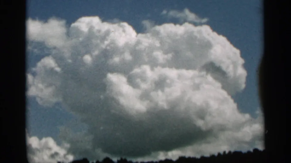 Duluth, Minnesota 1965 home-movie sky view with a bright cumulus cloud and low wooded horizon.
