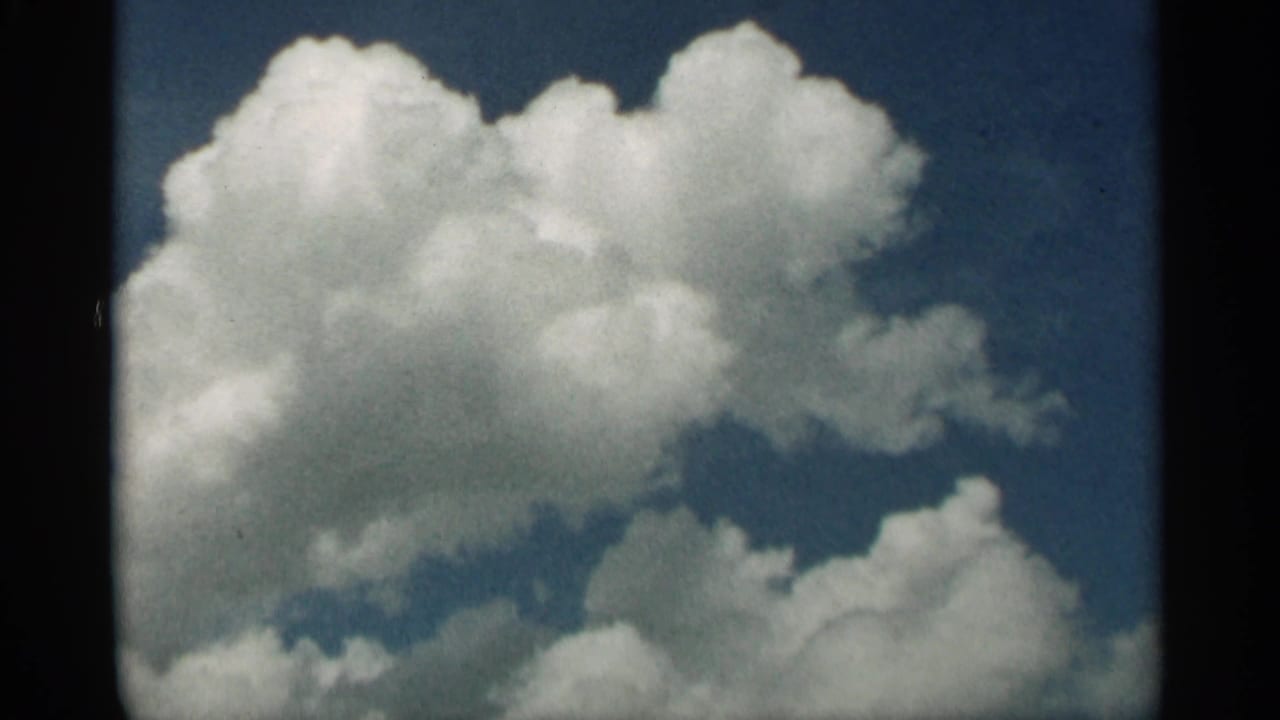 Bright cumulus clouds filling the sky within a dark film border.