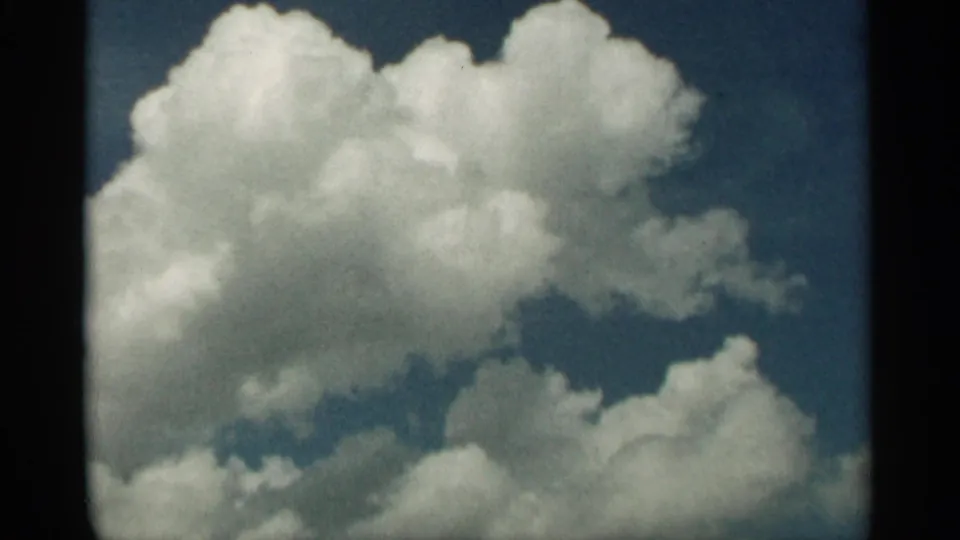1965 Duluth home-movie still with white cumulus clouds filling most of the frame against saturated blue sky.