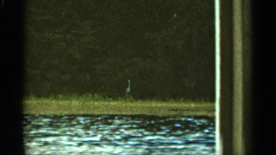 1965 Duluth-area home-movie view of a riverbank and water through dark framing, with a pale post or frame element near center.