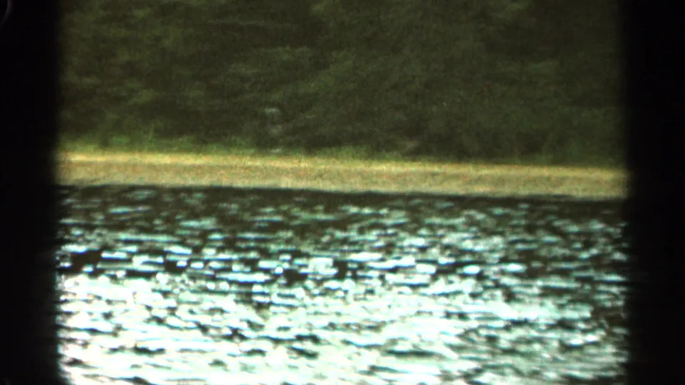 1965 Duluth-area river view with bright water reflections, a low shore, trees, and dark window framing at the sides.
