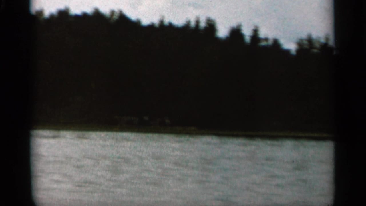 Wide lake surface with a dark wooded hillside and a small distant structure.