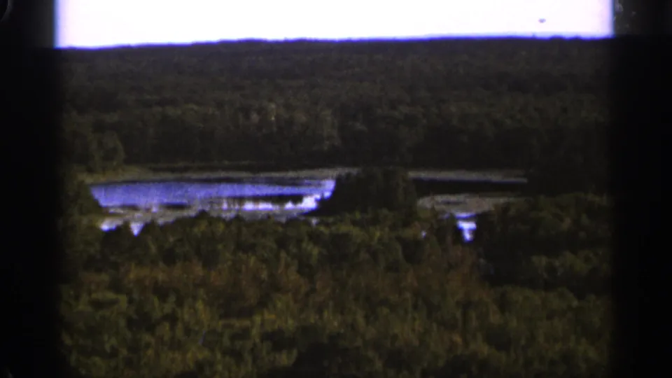 1965 Duluth-area 8mm frame with dense forest in the foreground and a reflective lake set below the horizon.