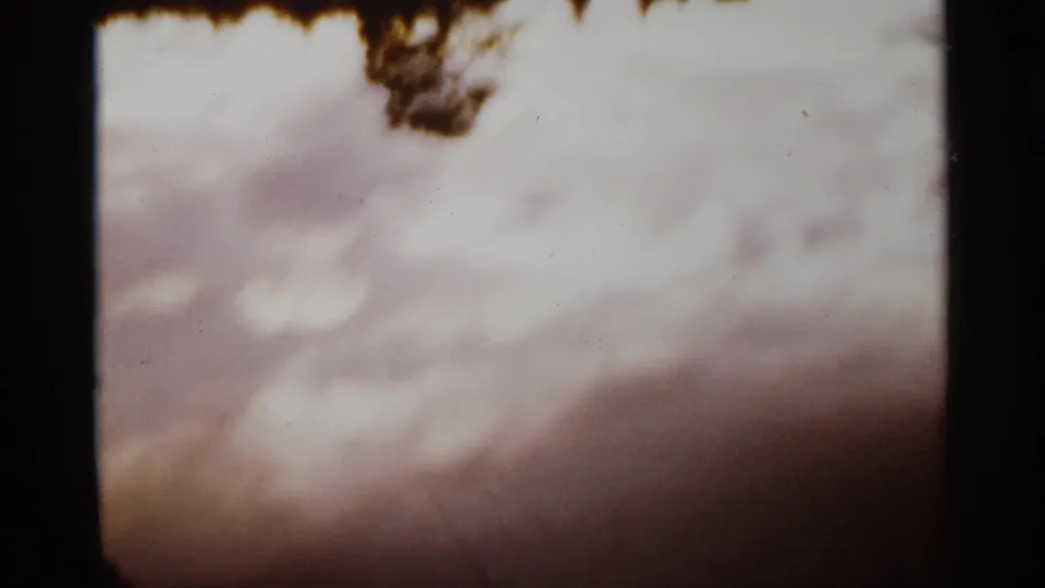 1965 Duluth 8mm frame of pale overcast sky with dark tree branches at the upper edge.