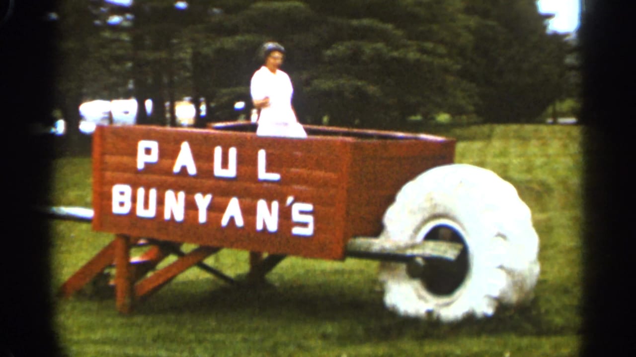 Woman in white standing in the wheelbarrow display with Paul Bunyan's lettering visible.