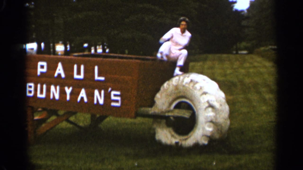 Woman climbing from the large Paul Bunyan wheelbarrow display near its oversized wheel.