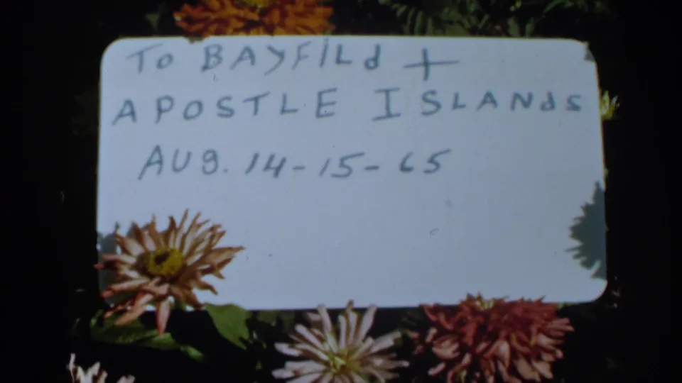 Close 8mm view of the Bayfield and Apostle Islands handwritten card dated Aug. 14-15-65, surrounded by flowers.