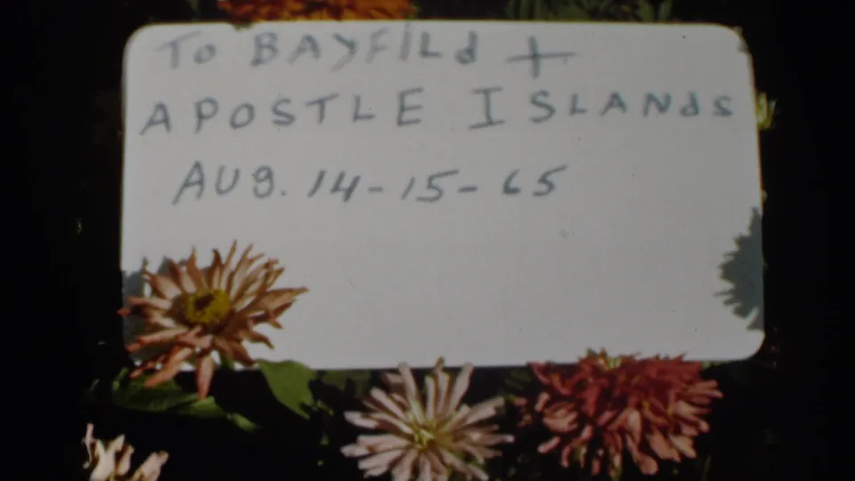 Final 1965 8mm frame showing a handwritten Bayfield and Apostle Islands card above chrysanthemums on a dark background.